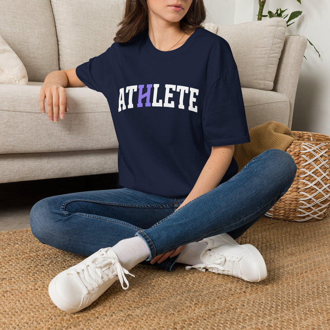 A woman sitting cross-legged on a woven rug in front of a beige sofa, wearing an oversized navy blue t-shirt with the word &